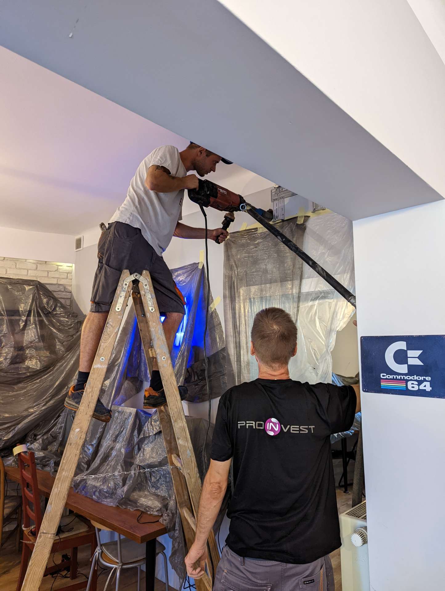 Instalator na drabinie w muzeum (w tle mural i znak C=64)